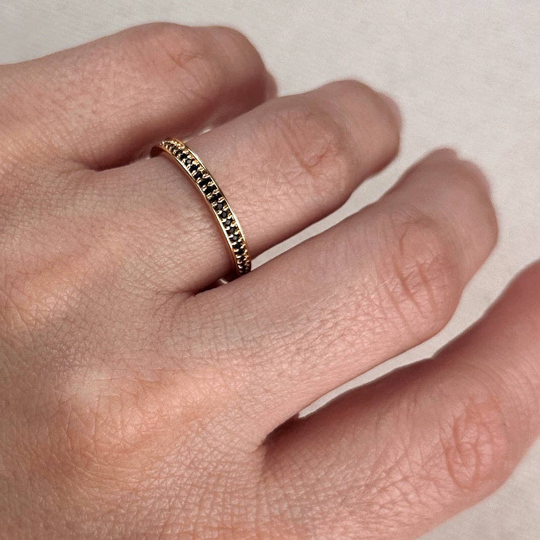 Gold ring with black stones on a finger against a neutral background