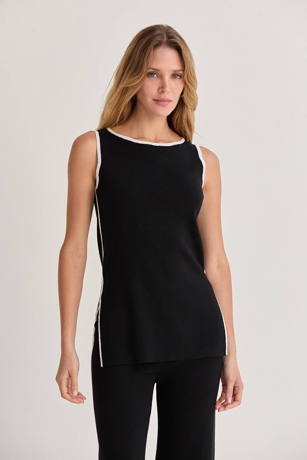 Woman wearing a black sleeveless top with white trim on a light gray background