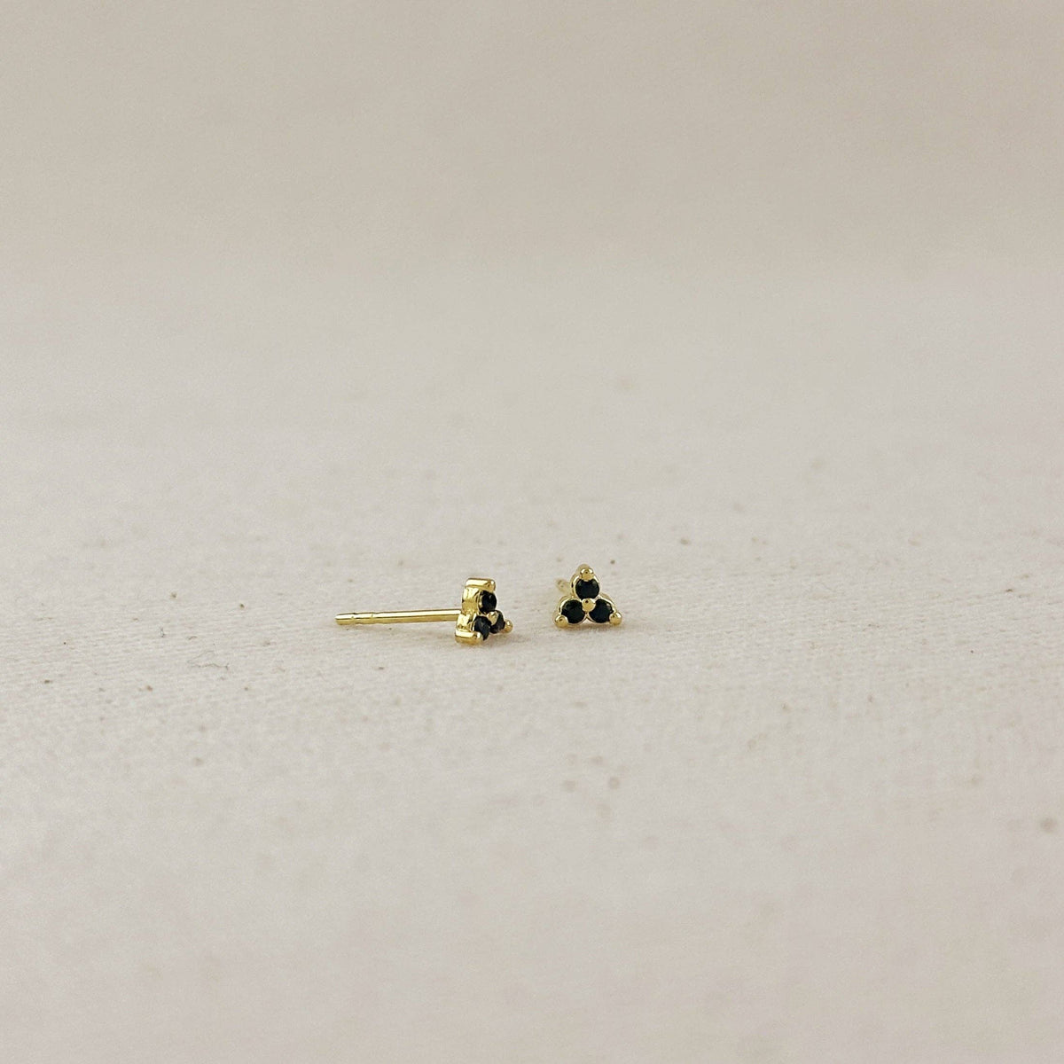 Gold earrings with black stones on a light gray background