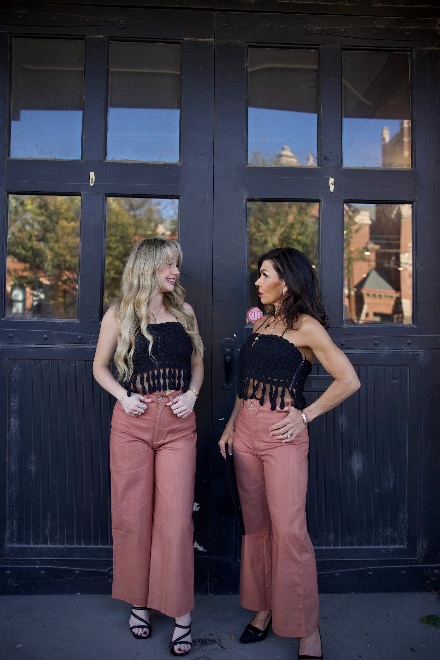 Two women standing in front of a dark wooden door with glass panels.