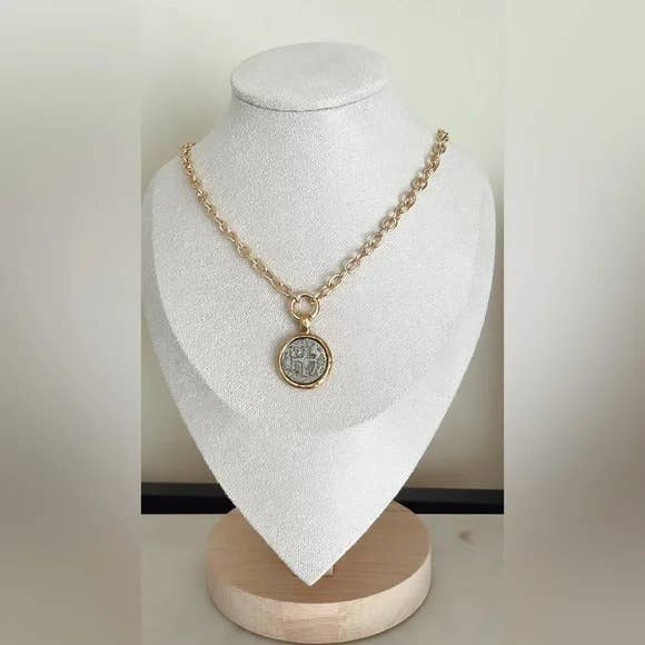 A gold chain necklace with a round pendant featuring an embossed religious design, displayed on a white jewelry bust.