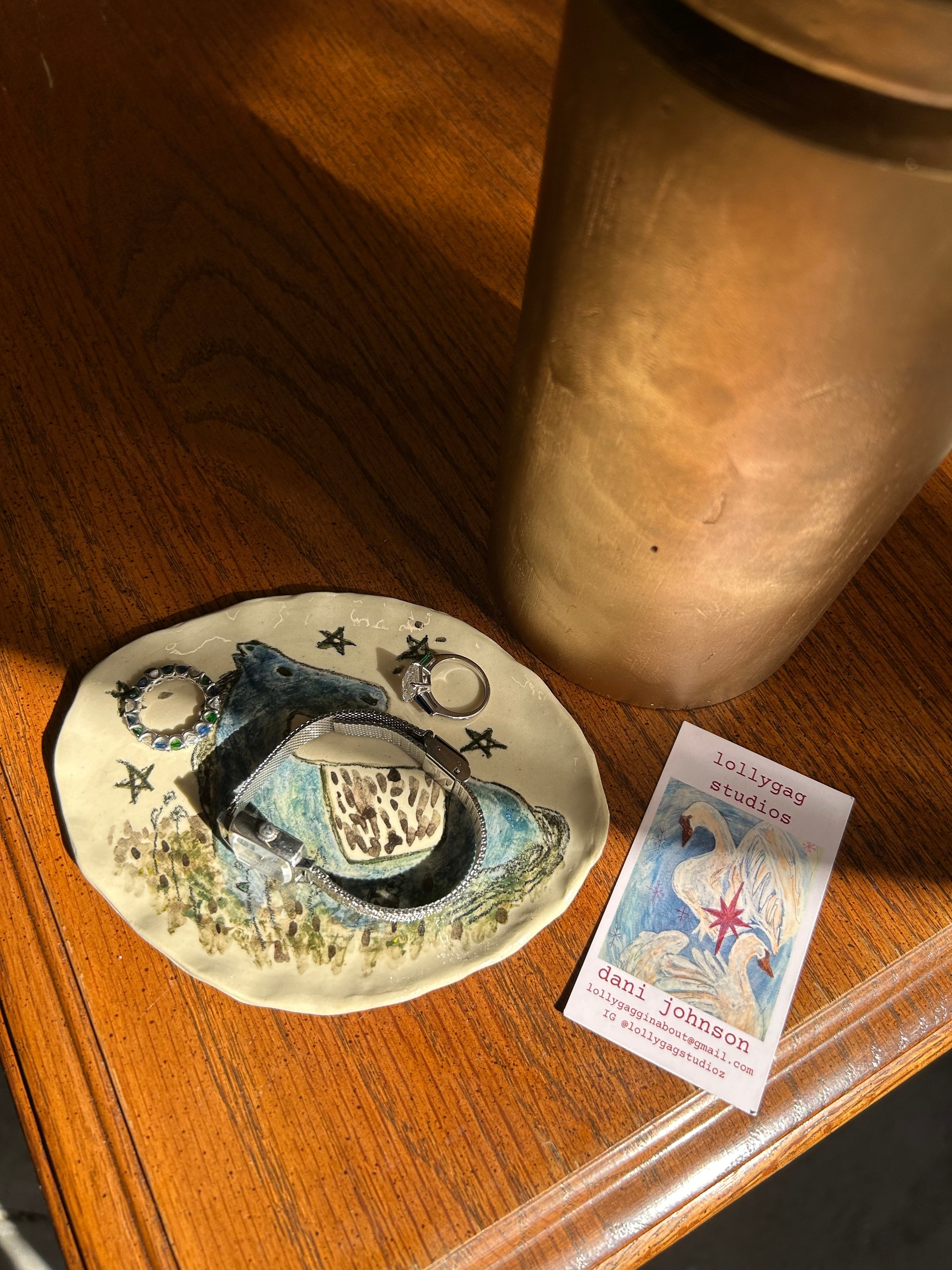 Decorative plate with celestial design on a wooden surface next to a metallic container and a colorful card.