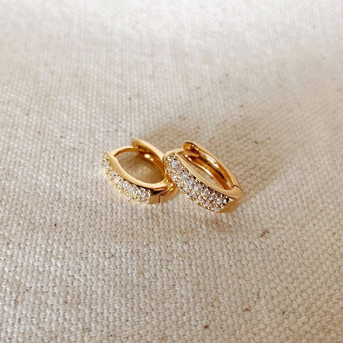 Gold hoop earrings with embedded stones on a beige fabric background