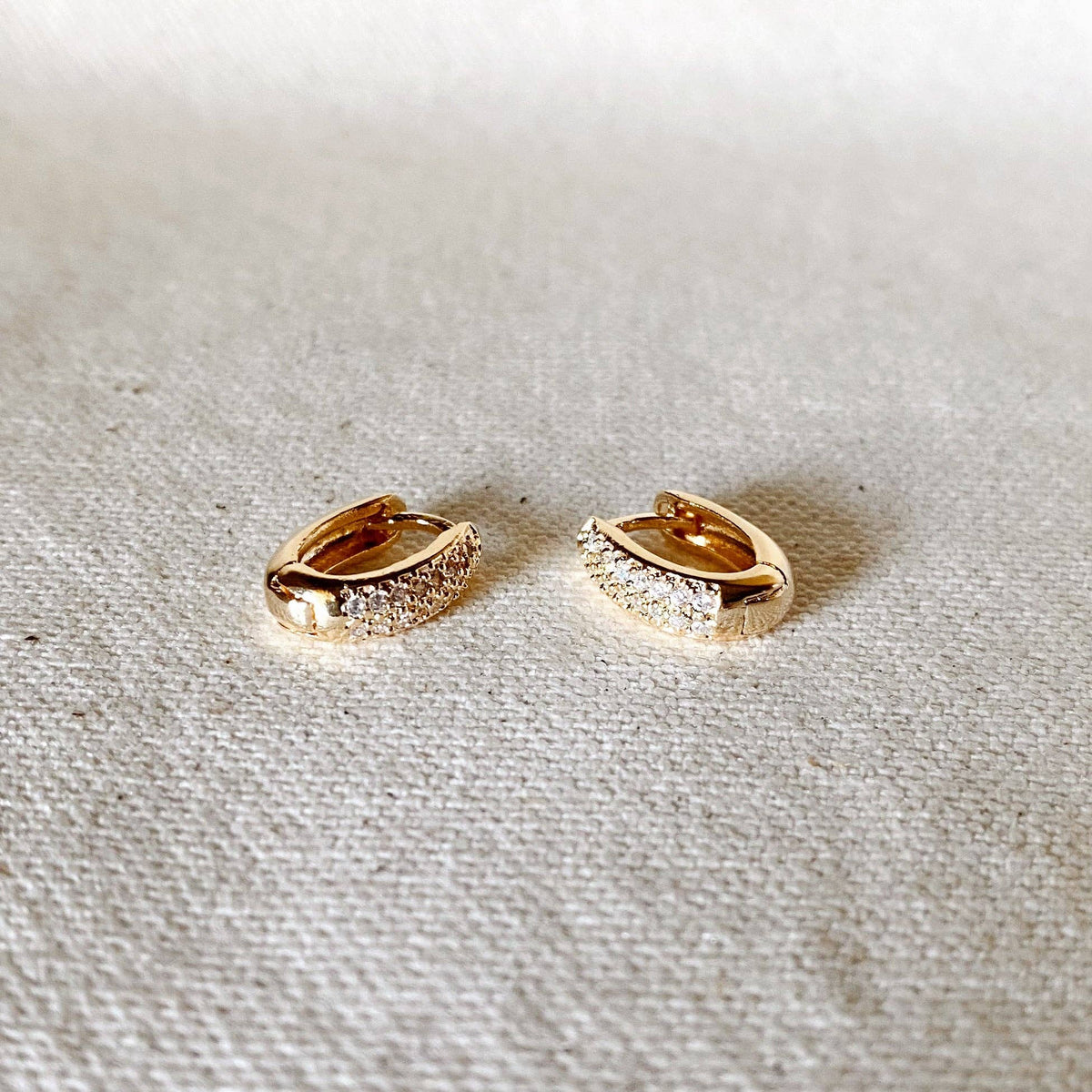 Gold hoop earrings with diamond accents on a light fabric background