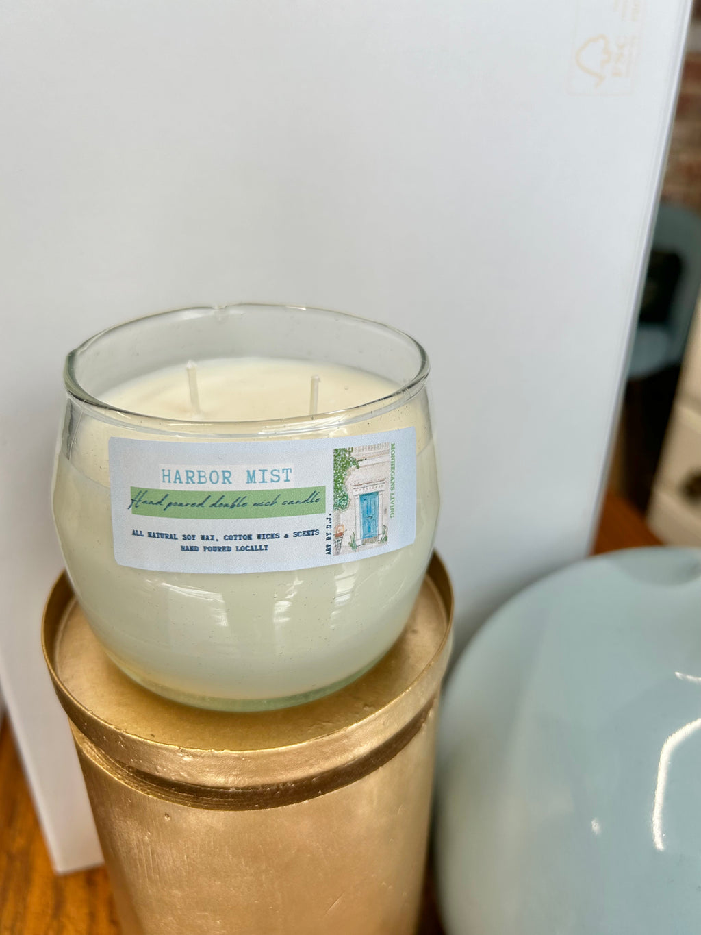 Candle in a glass jar with a label on a gold stand against a white background