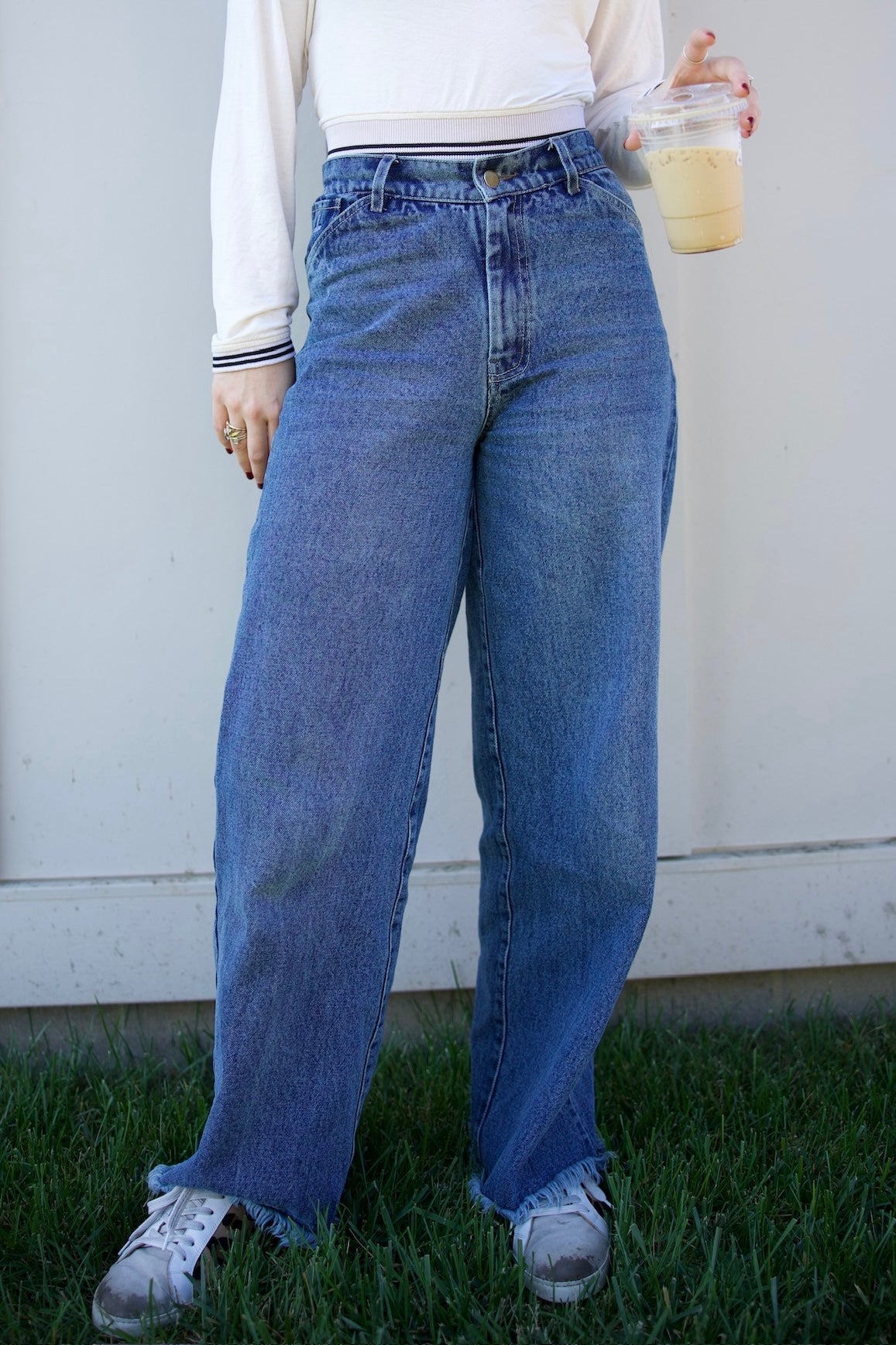 Person wearing blue jeans and a white shirt, standing on grass with a plain background