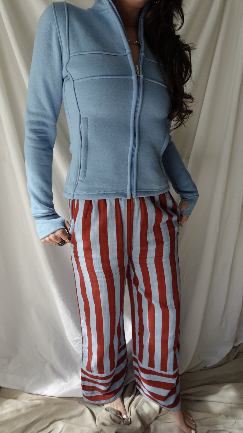 Person wearing a blue hoodie and red and white striped pants on a bed.