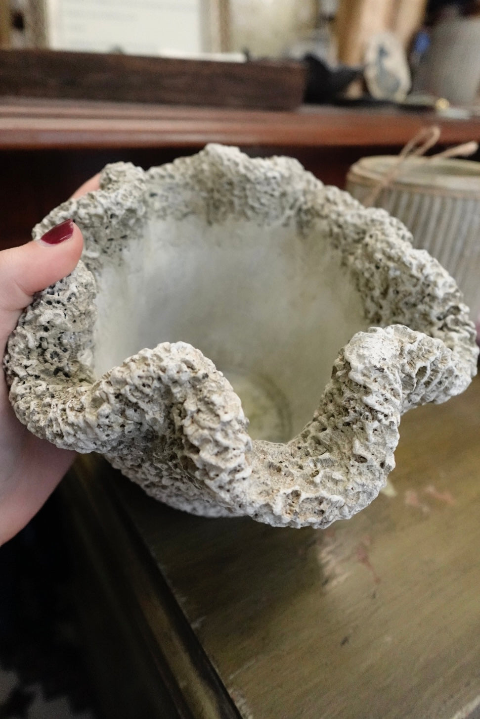 Hand holding a textured stone bowl on a reflective surface