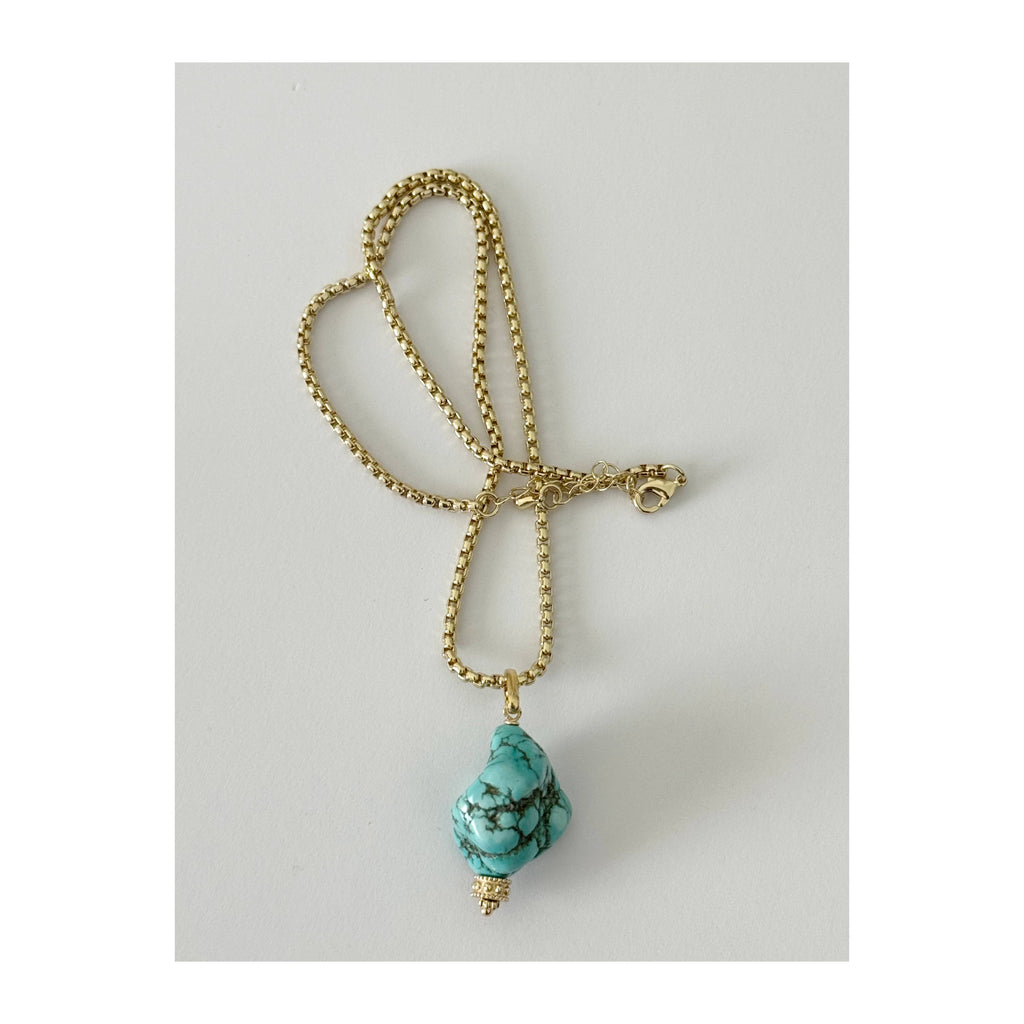 A gold beaded chain necklace with a teardrop-shaped turquoise stone pendant, displayed on a light gray background.