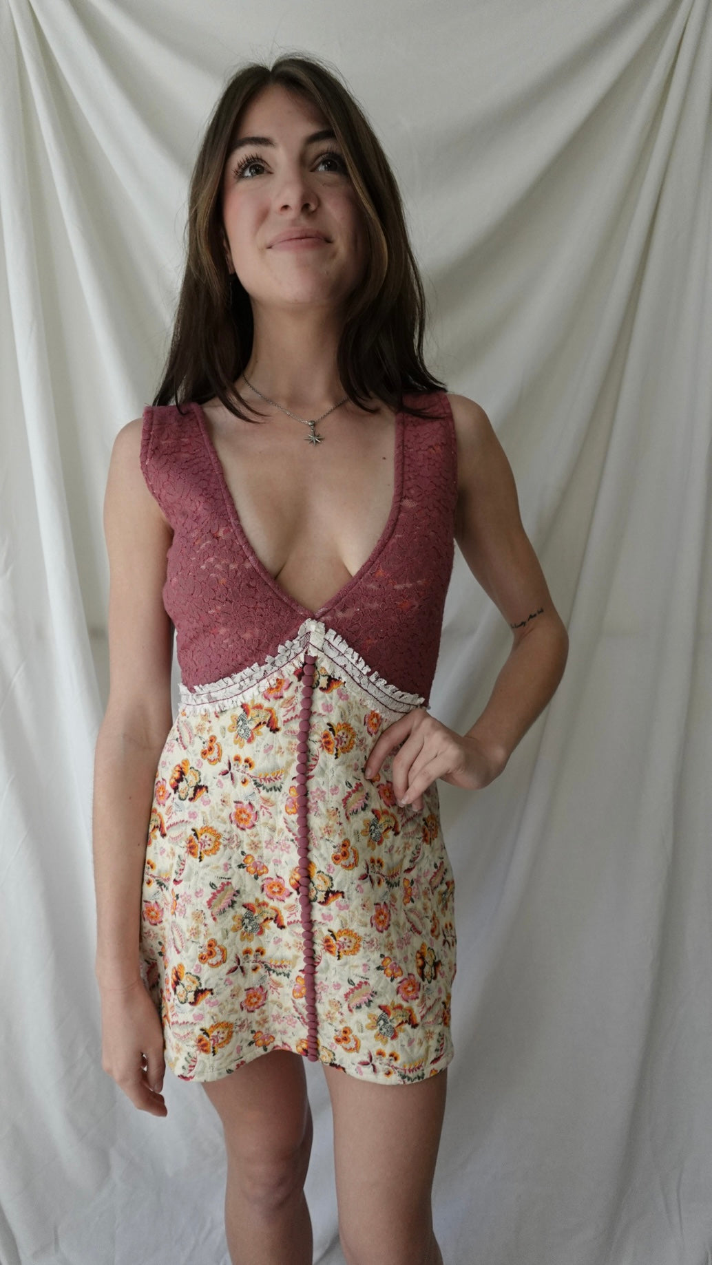 Woman wearing a floral dress over a maroon lace top against a plain background