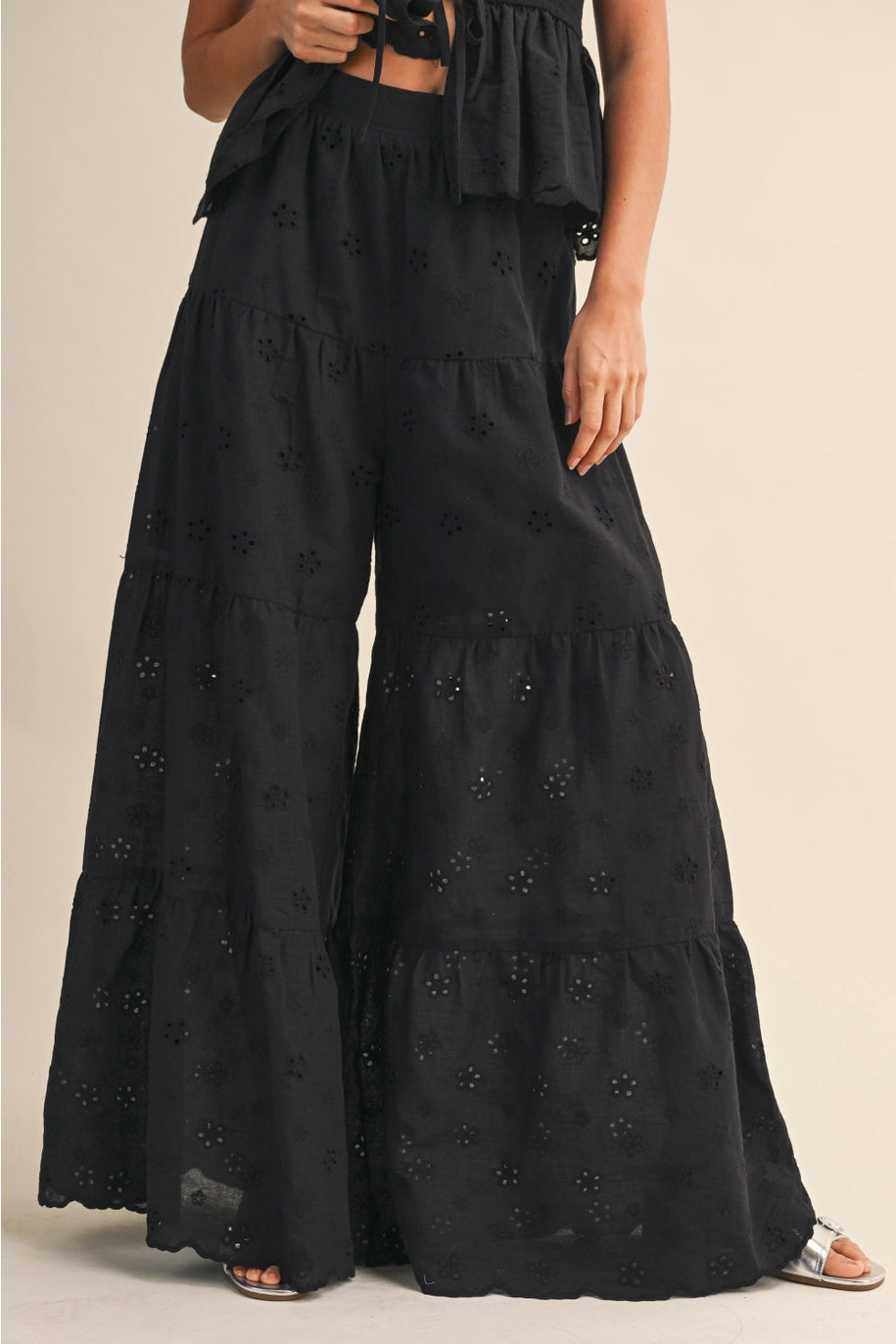 Black embroidered wide-leg pants worn by a person on a beige background