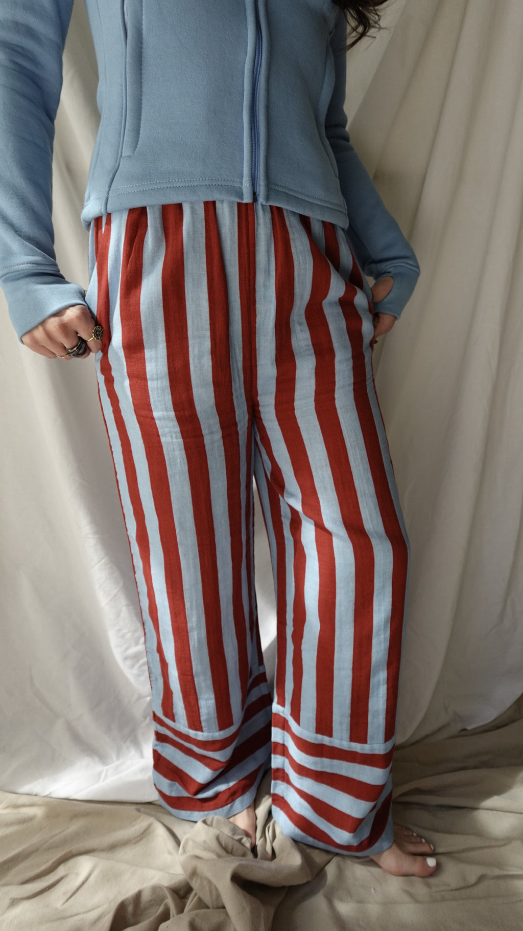 Person wearing red and white striped pants with a blue jacket on a neutral background