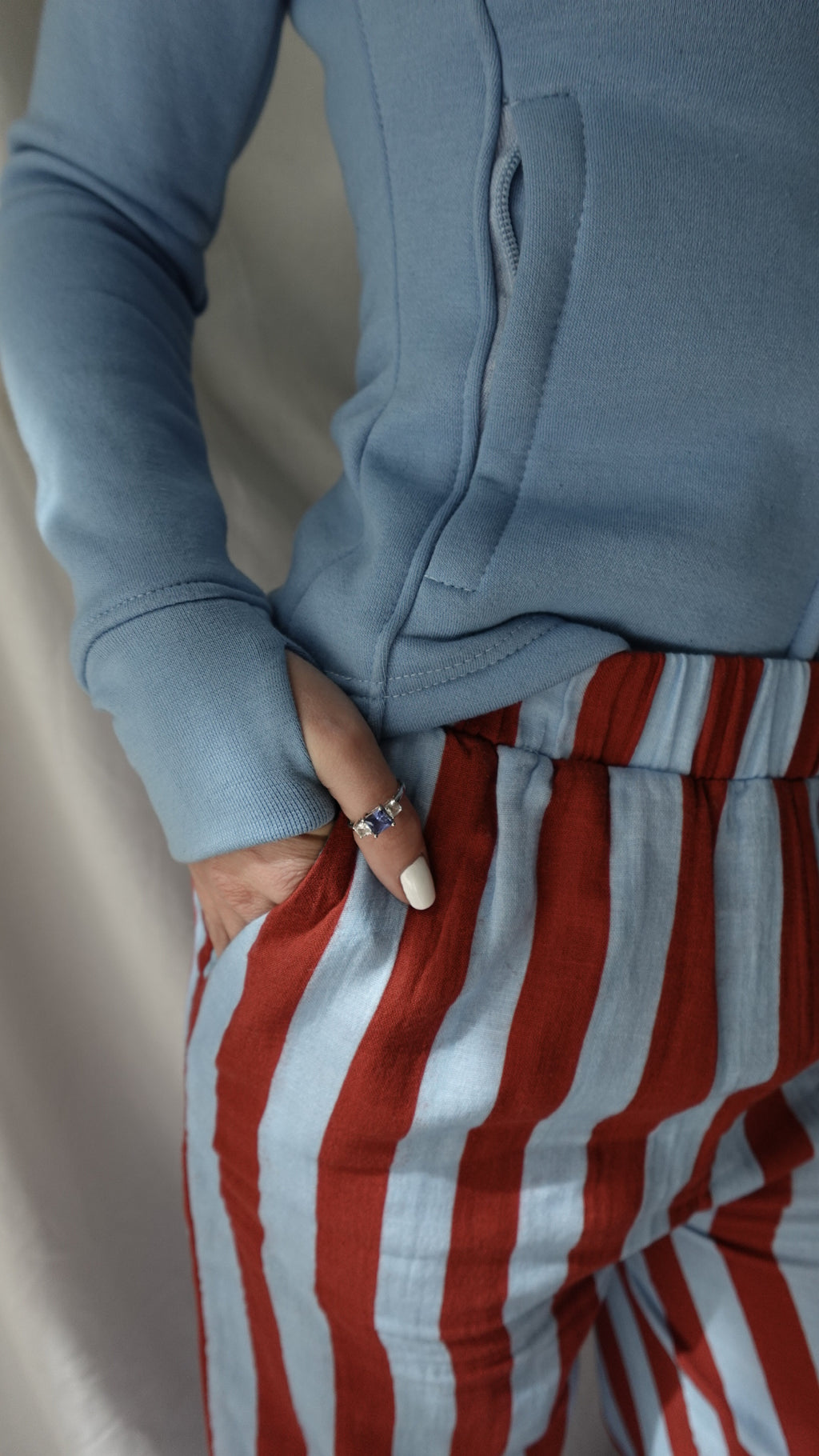Person wearing a blue sweatshirt holding a red and white striped fabric.