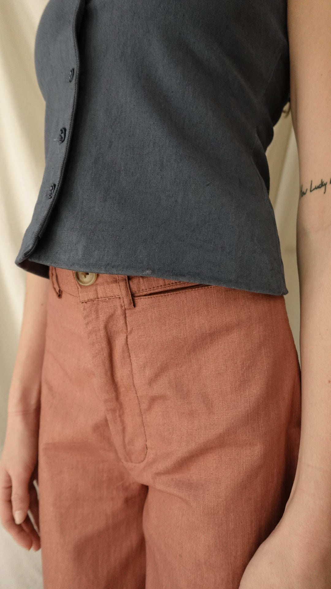 Close-up of a person wearing a dark shirt and brown pants on a neutral background