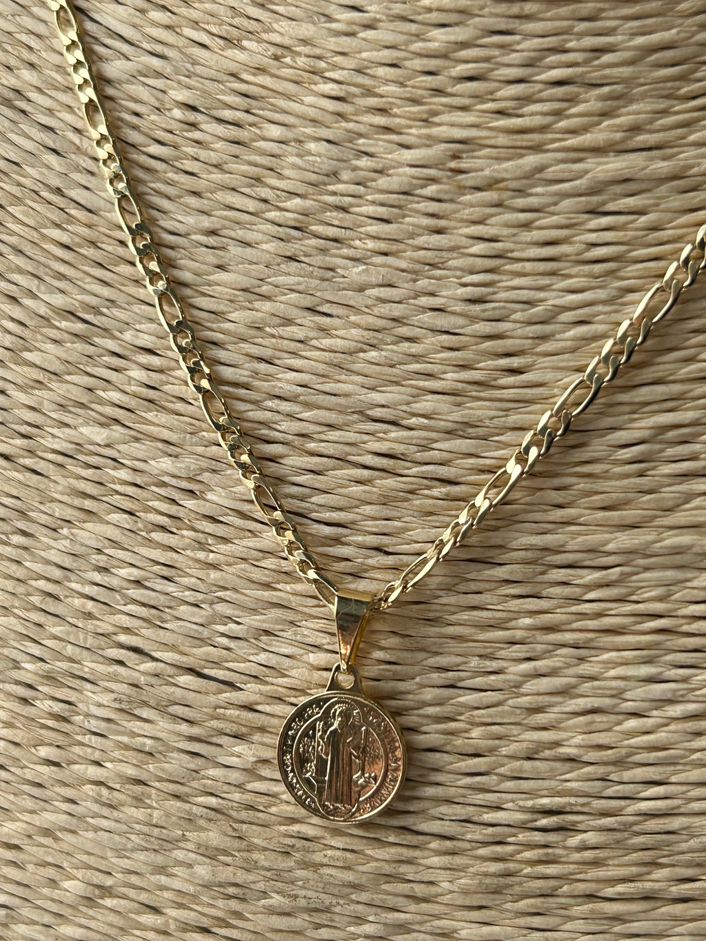 Gold necklace with a round pendant on a textured beige surface