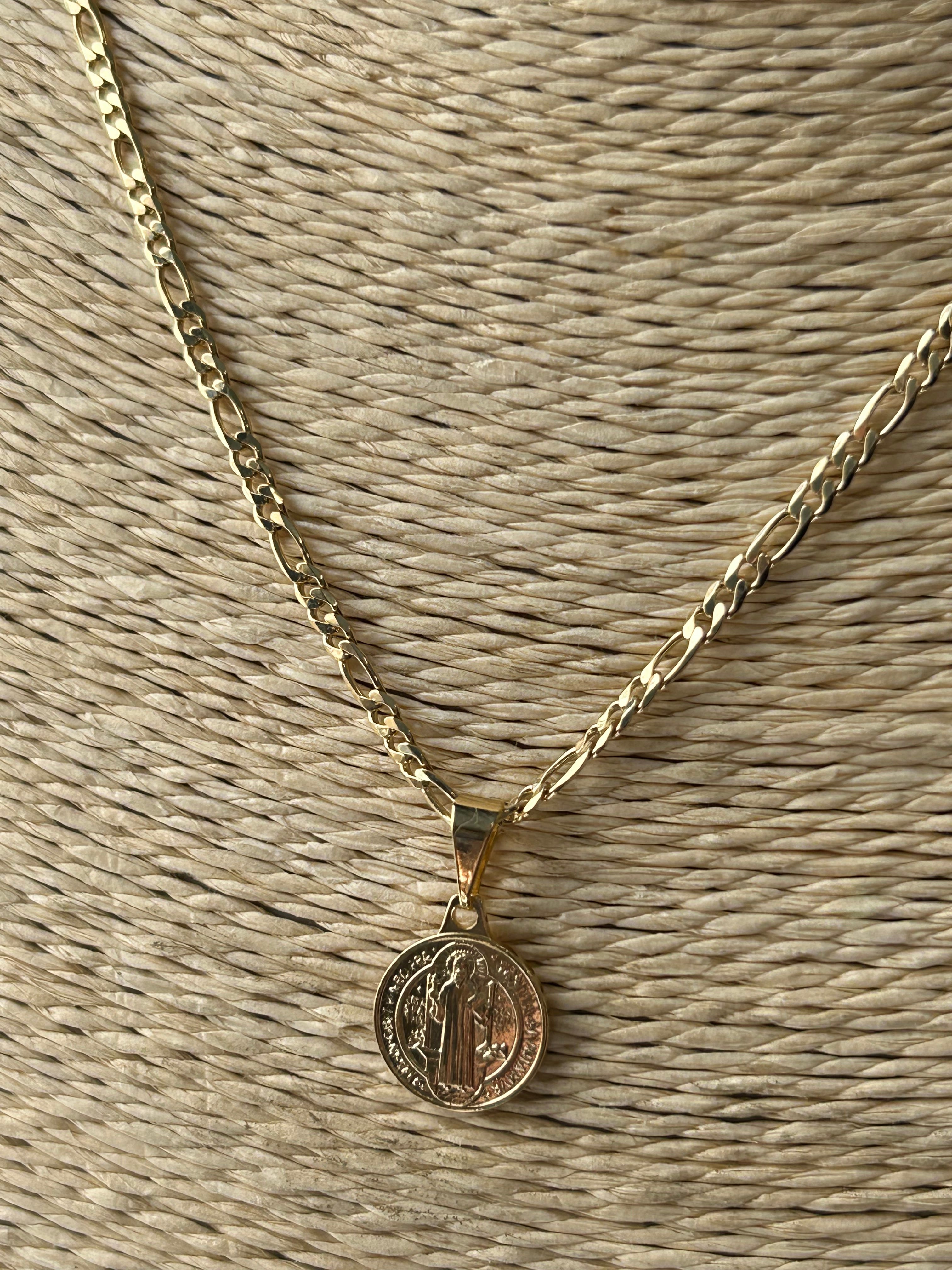 Gold necklace with a round pendant on a textured beige surface