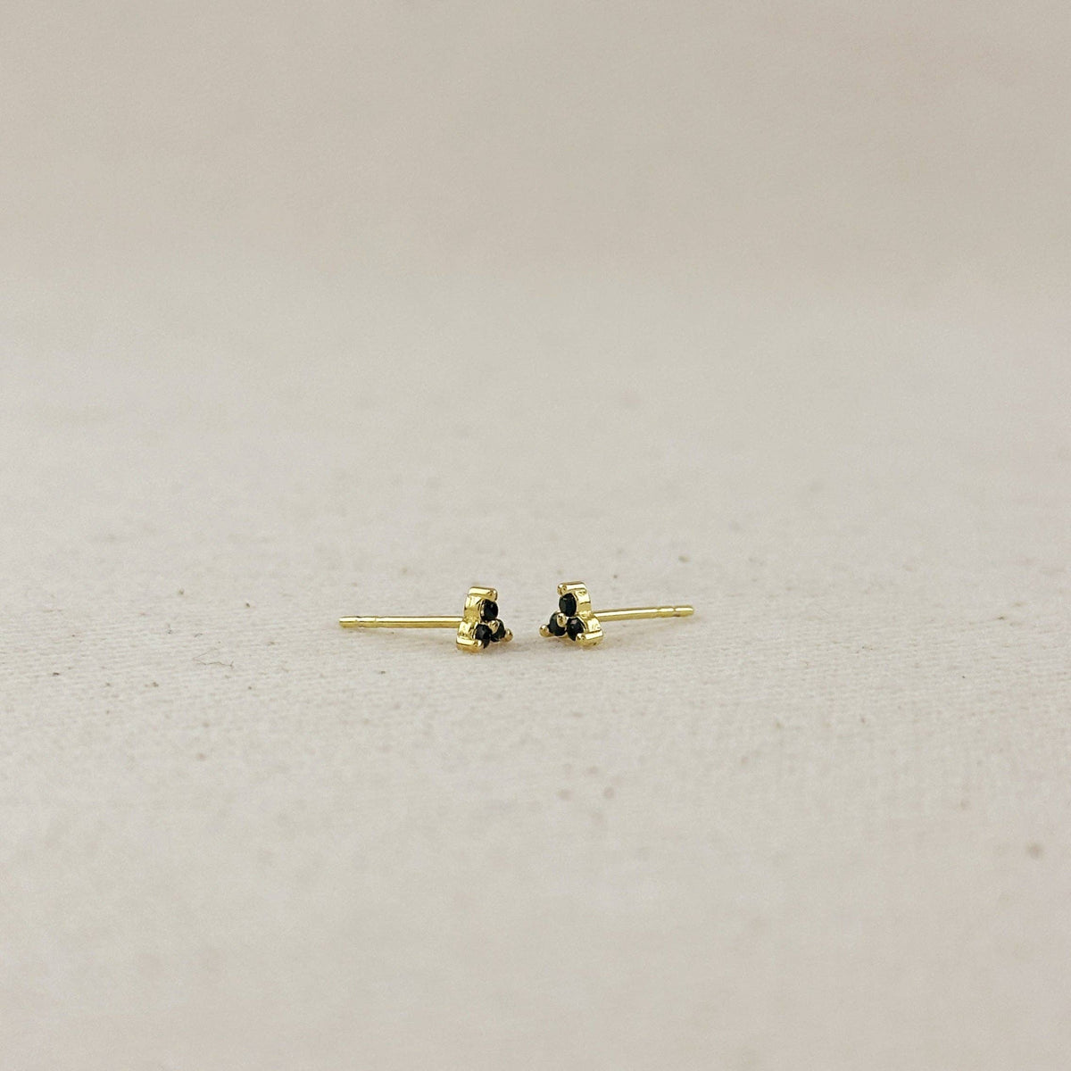Gold earrings with black stones on a light gray background