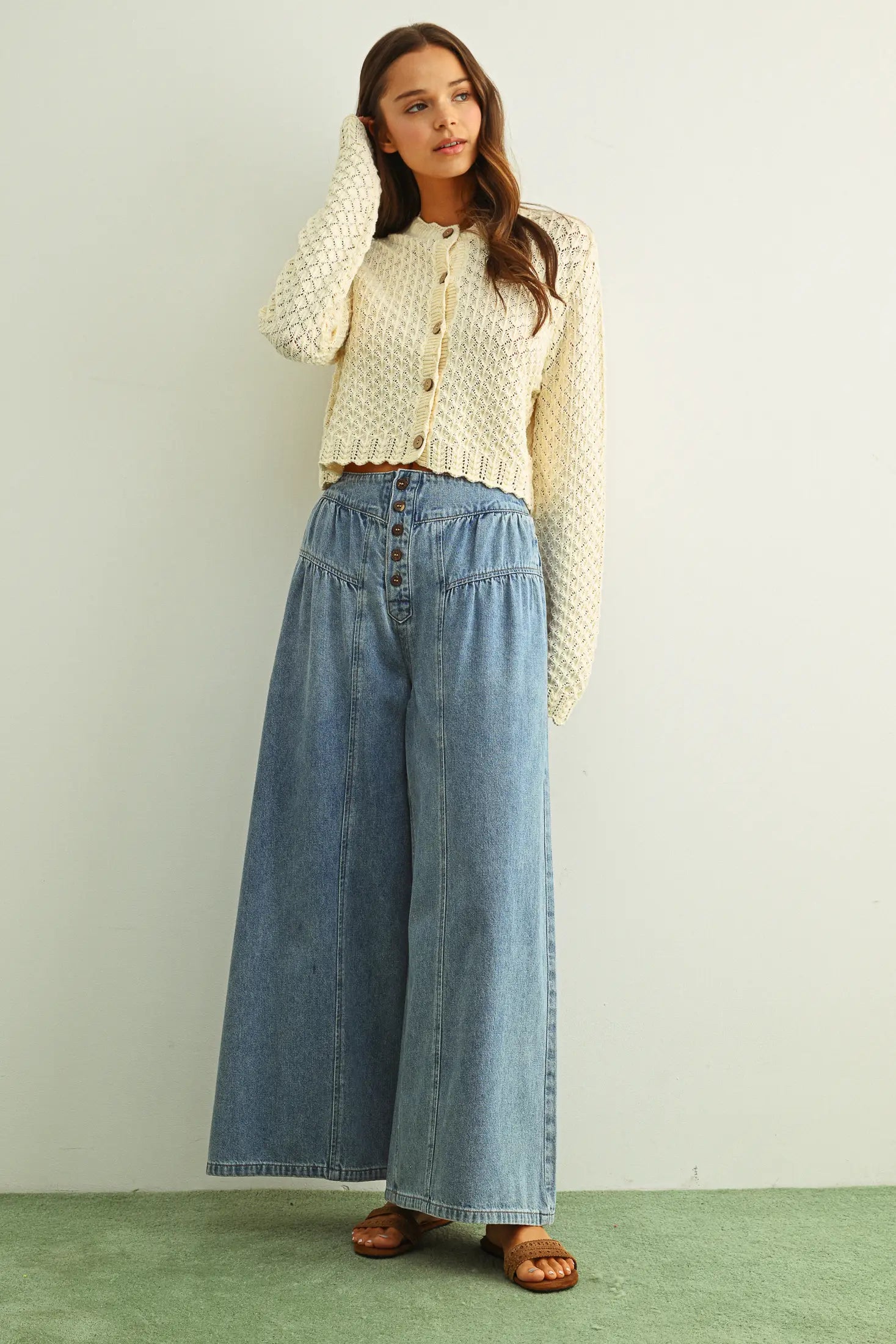 Woman wearing a beige patterned blouse and blue denim wide-leg pants against a plain background