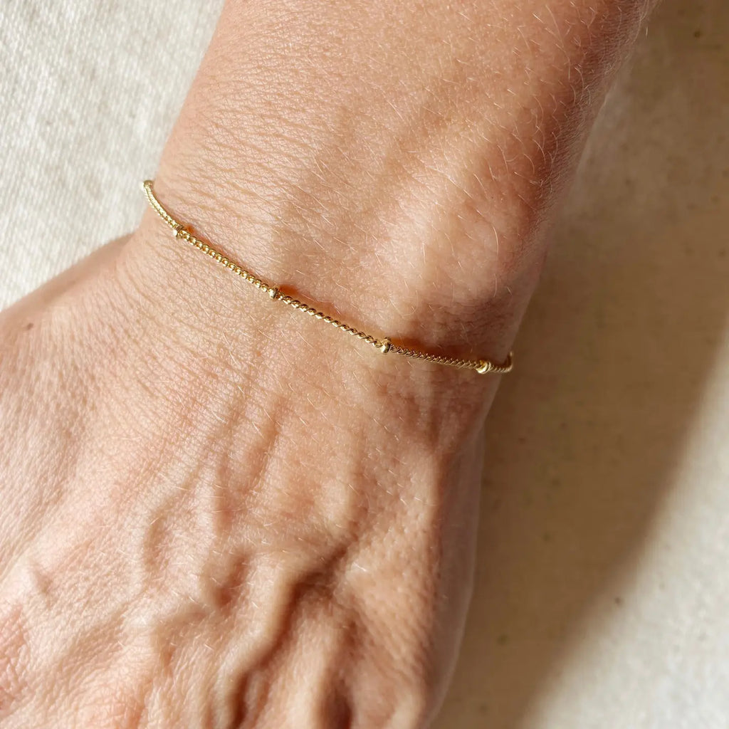 Gold bracelet on a wrist against a neutral background