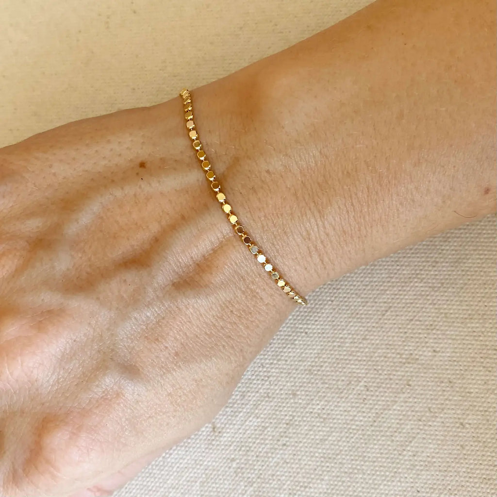 Gold bracelet on a wrist with a neutral background