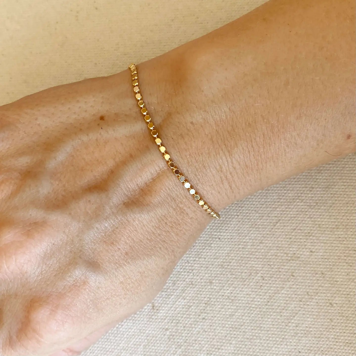 Gold bracelet on a wrist with a neutral background