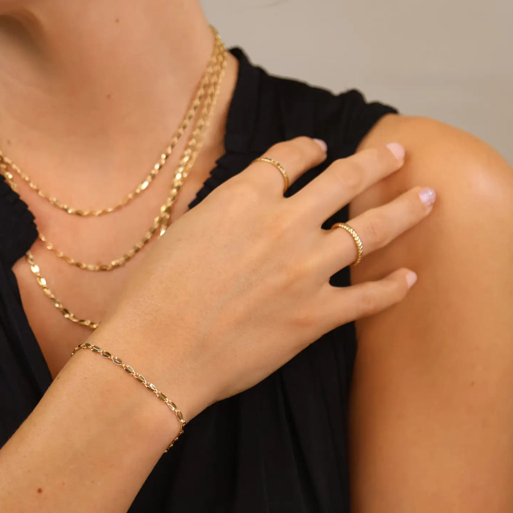 Close-up of a person wearing gold jewelry including a necklace, ring, and bracelet.
