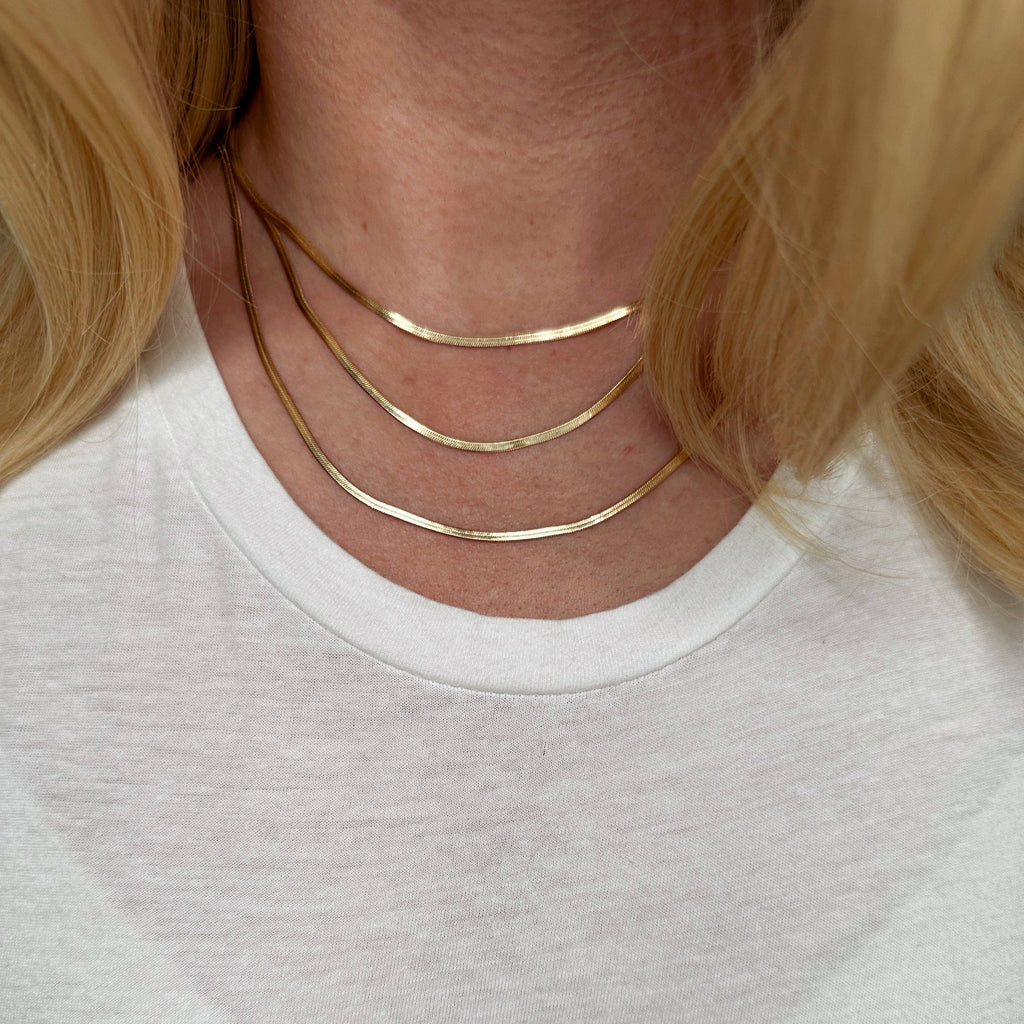 Close-up of a person wearing a gold necklace with a plain background