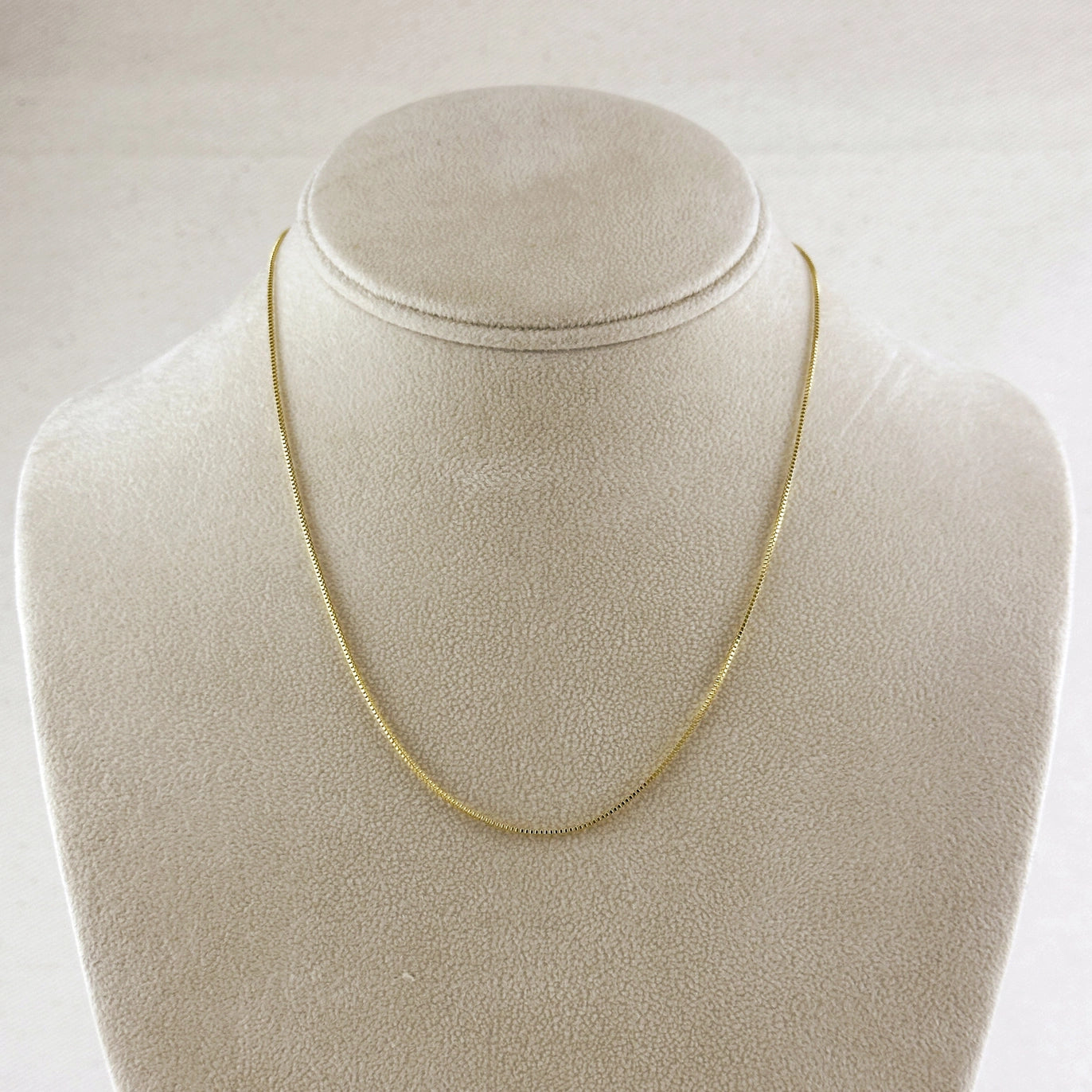 Gold chain necklace on a beige mannequin bust against a white background