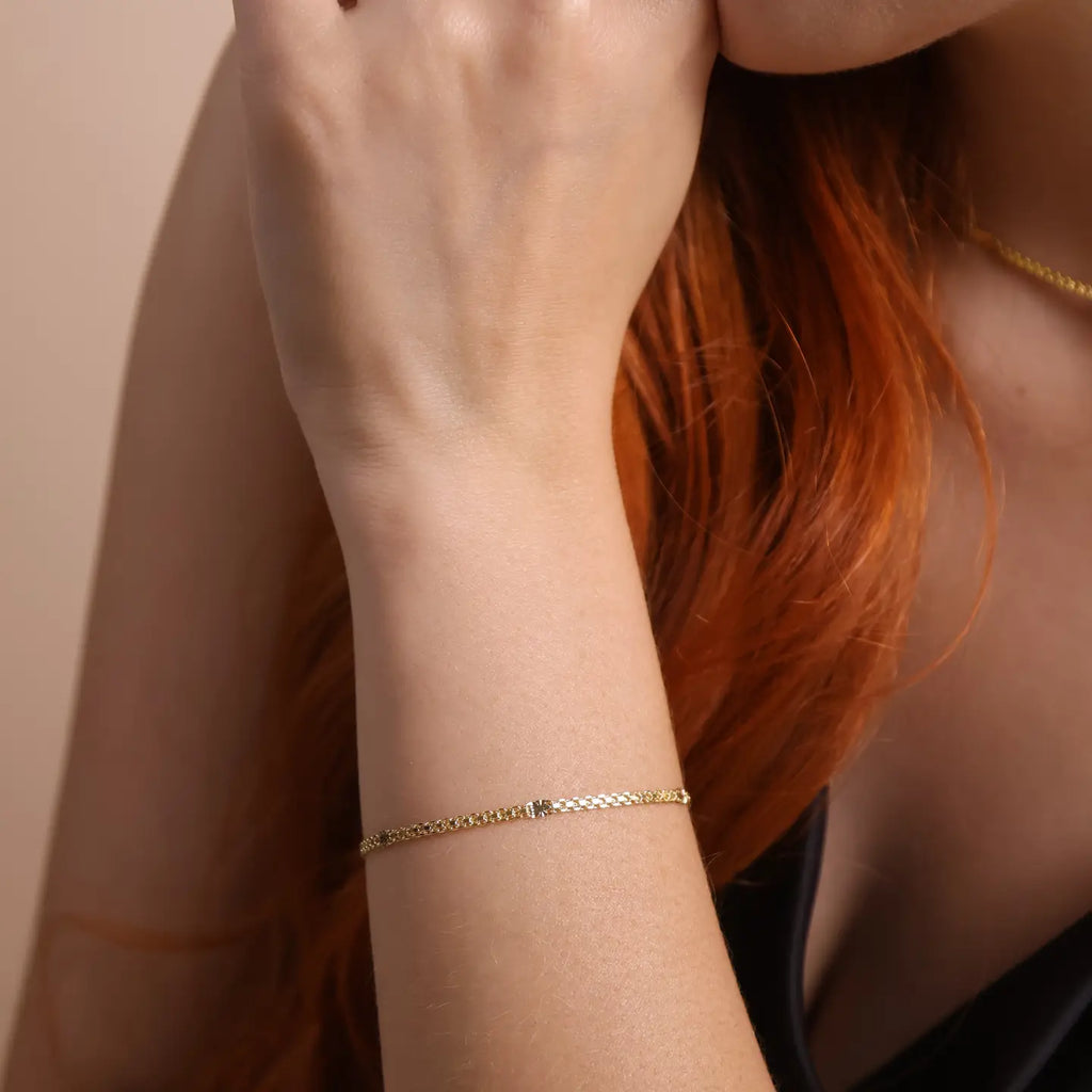 Close-up of a person's wrist wearing a gold bracelet against a neutral background