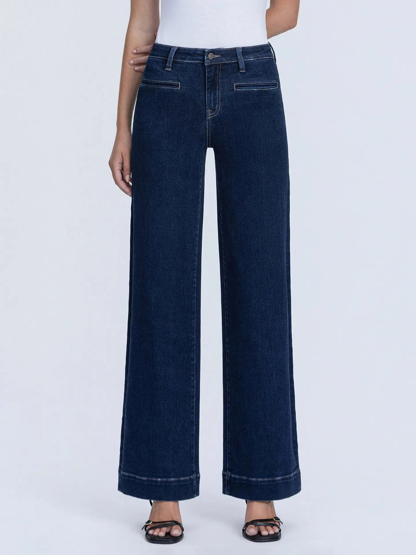 A model wearing dark blue wide-leg denim jeans with a white top and black sandals, shown from the waist down against a light gray studio background.