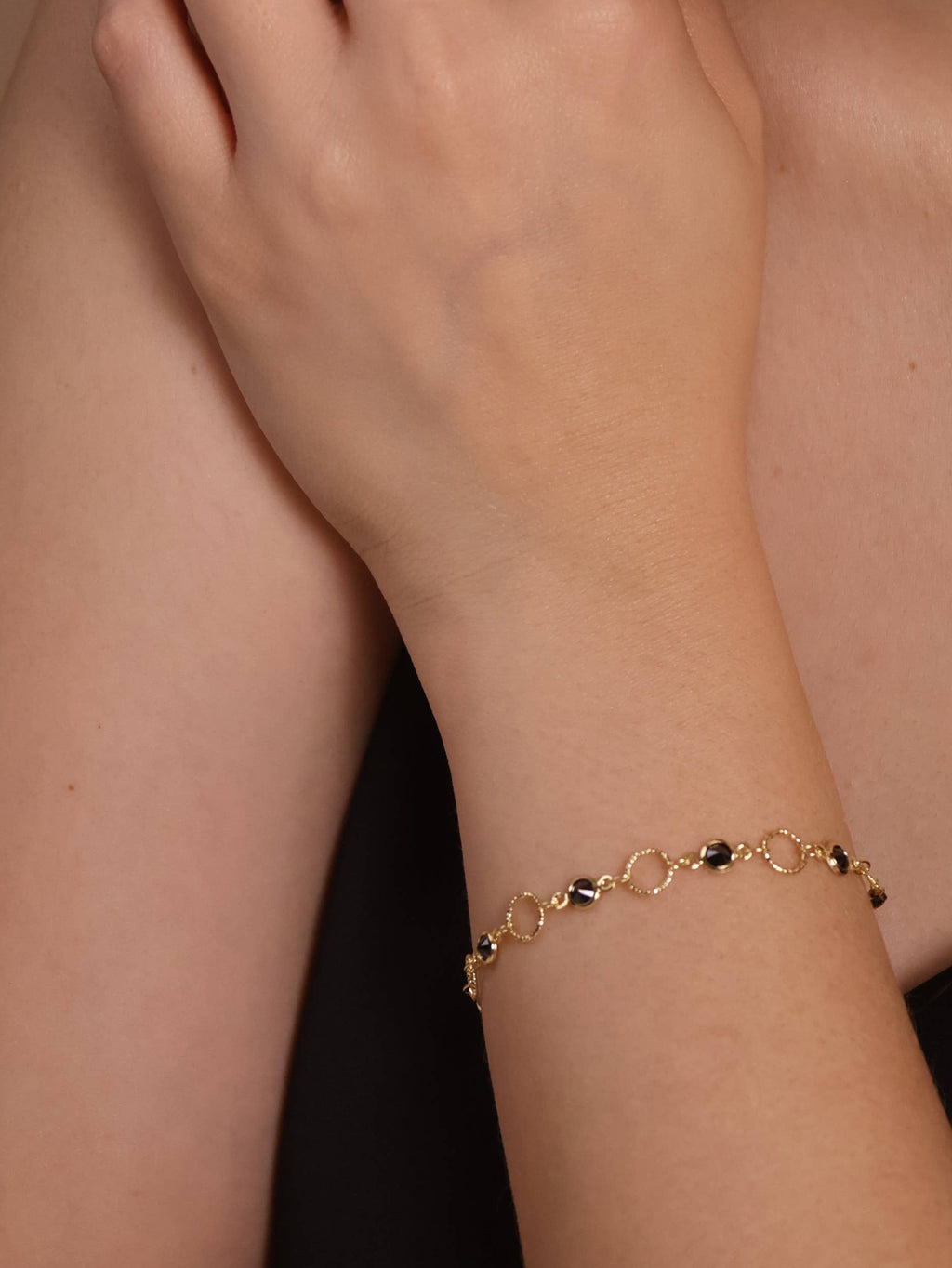 Close-up of a person wearing a gold bracelet and necklace on a beige background