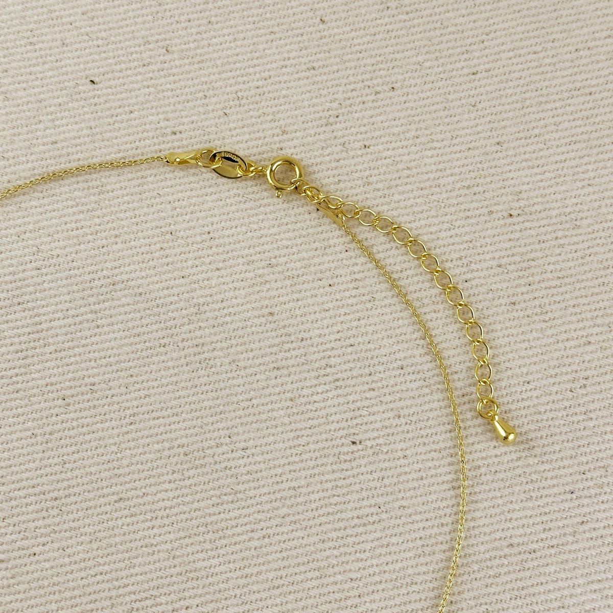 Close-up of a gold chain necklace with a lobster clasp and extender chain, laid on a textured beige fabric background.