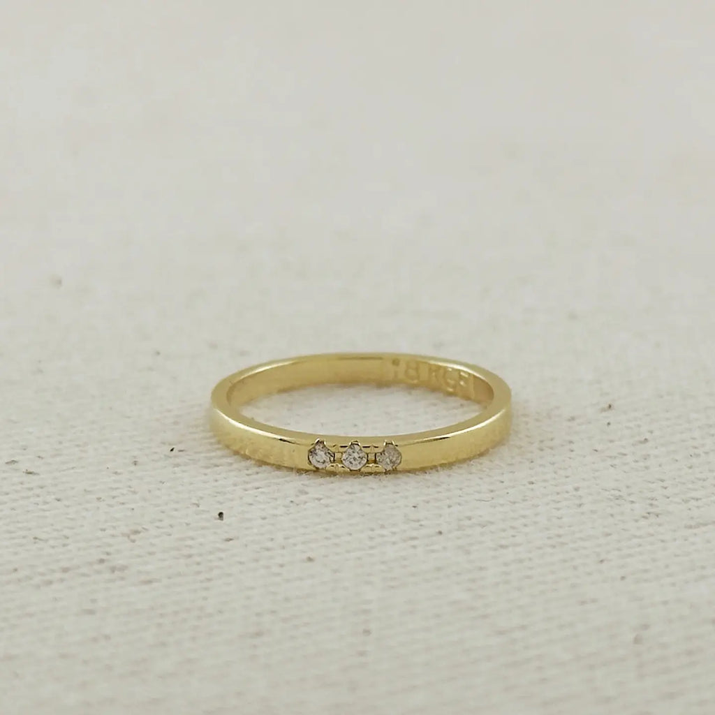 Gold ring with three diamonds on a light beige fabric background