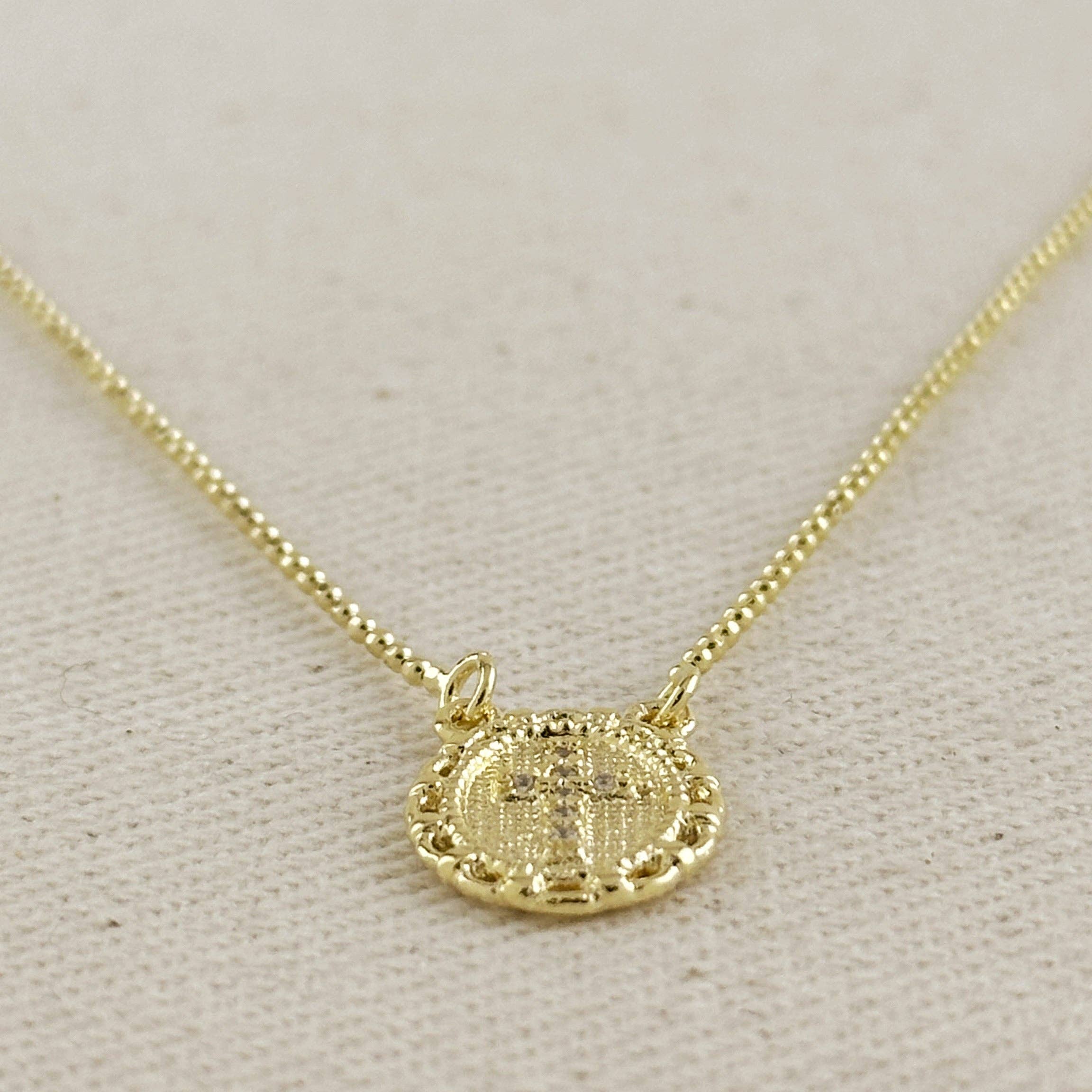 Gold necklace with a circular pendant on a light gray background