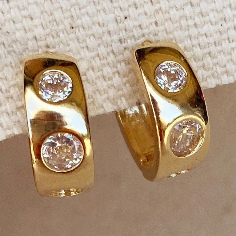 Gold hoop earrings with embedded diamonds on a textured surface
