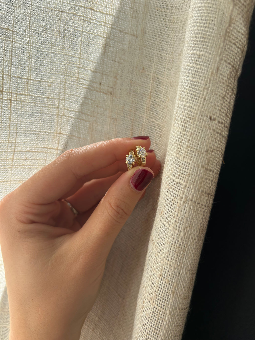 Hand wearing a gold ring with a diamond on a textured fabric background