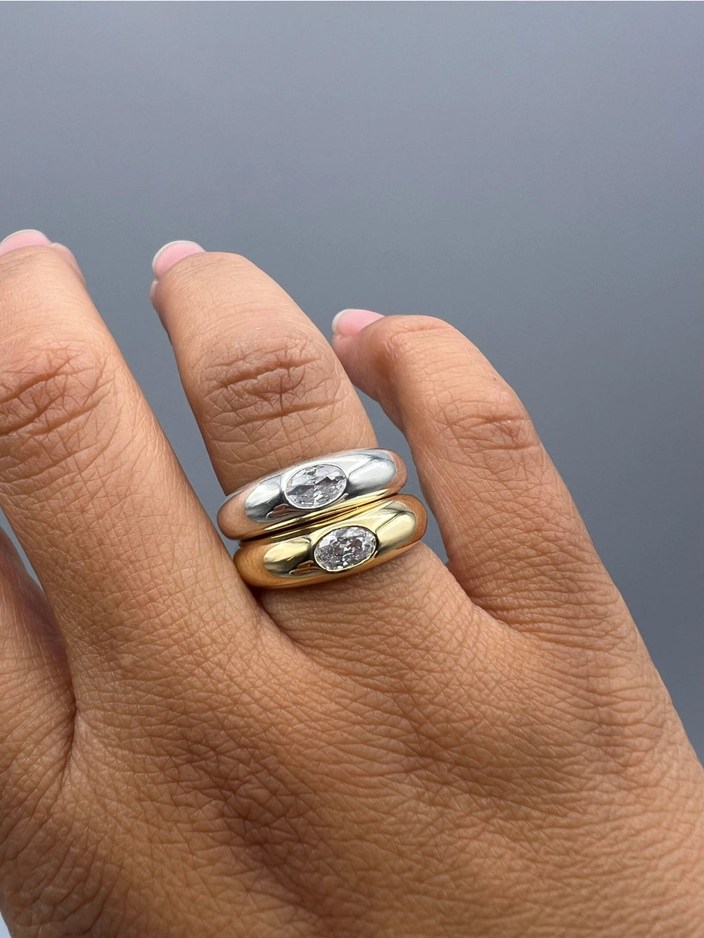 Hand wearing two gold rings with gemstones on a gray background