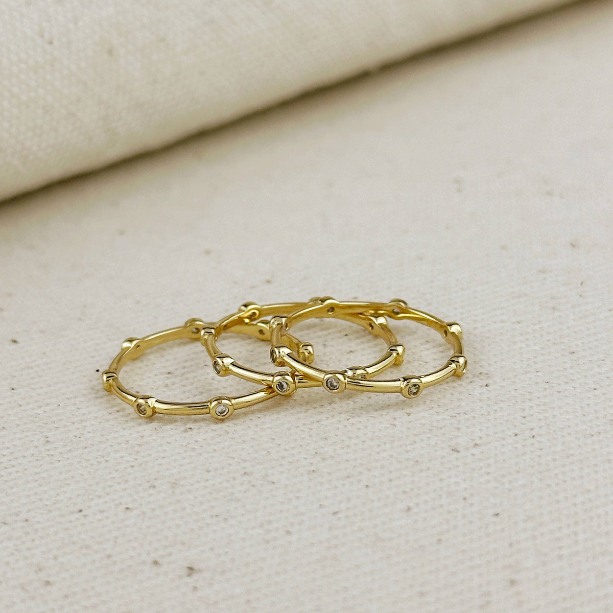 Three gold hoop earrings with small stones on a beige fabric background