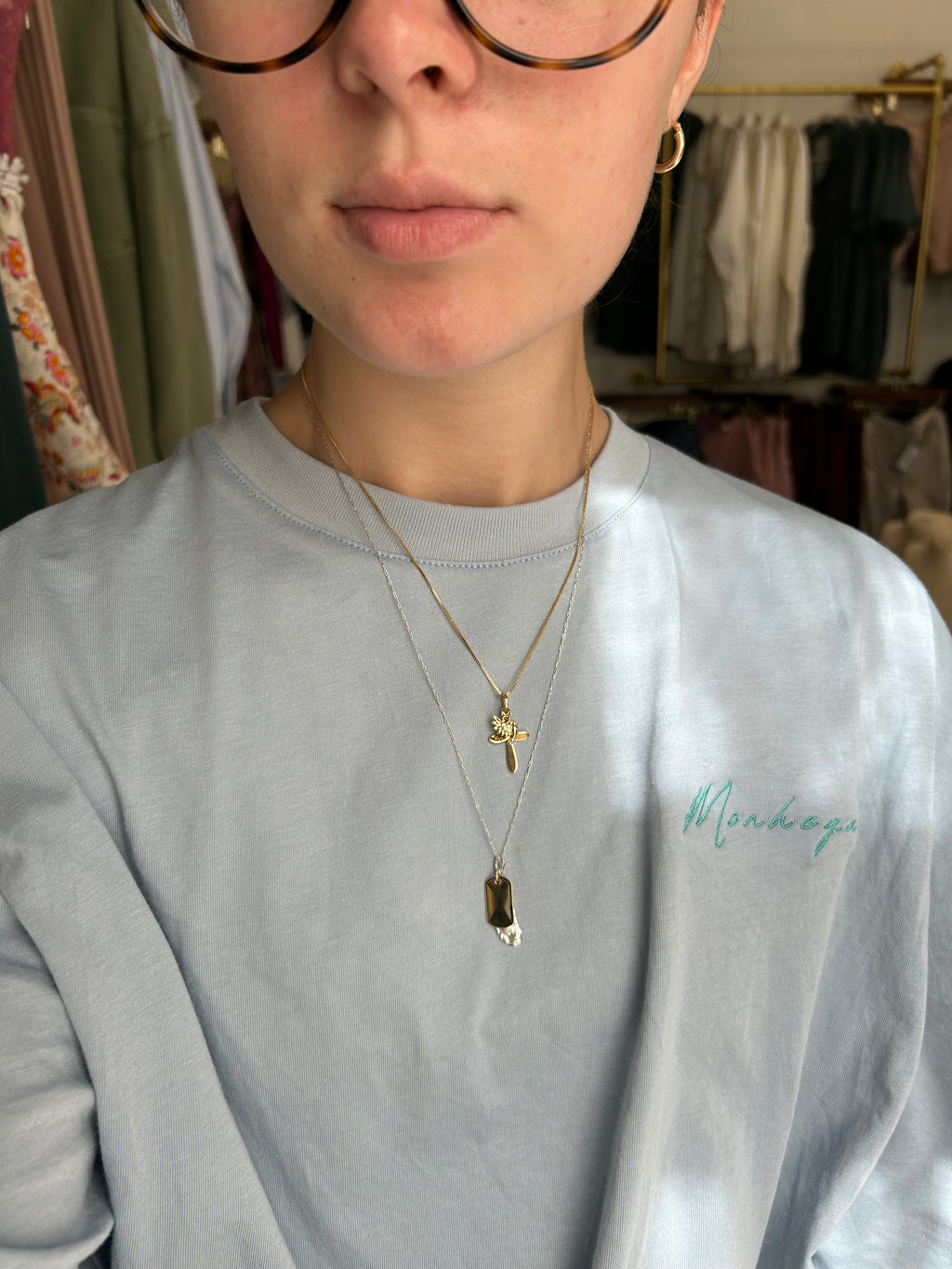 Person wearing a light gray shirt with a brand logo and gold necklaces.