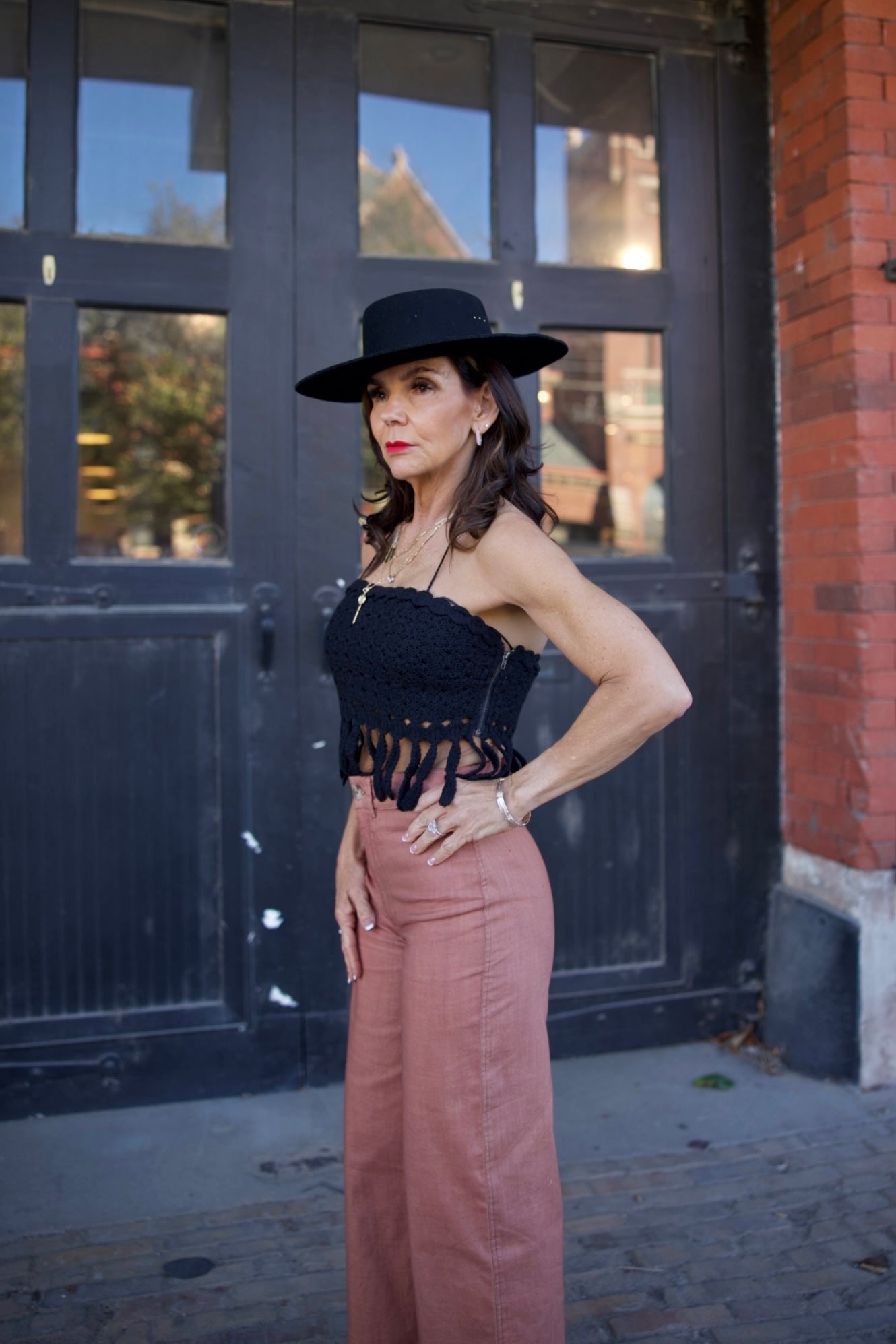Woman in black hat and black top with fringe standing in front of a large door.