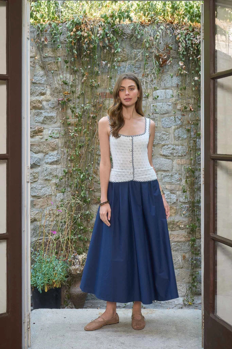 Woman wearing a white top and blue skirt standing in front of a stone wall.