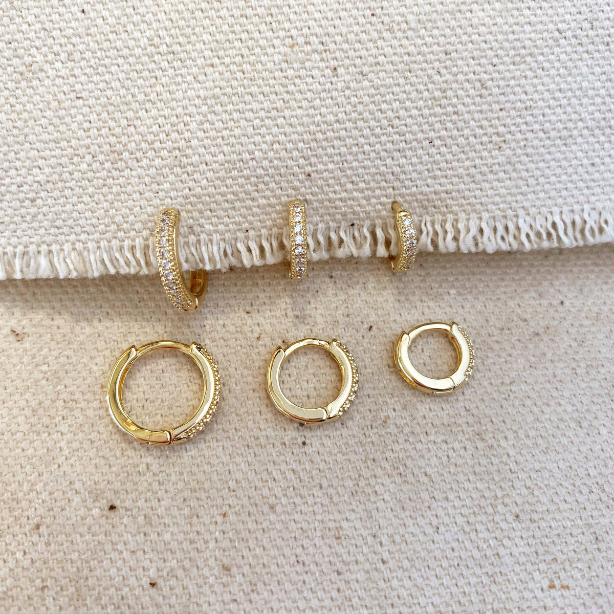 Set of gold hoop earrings on a textured beige surface