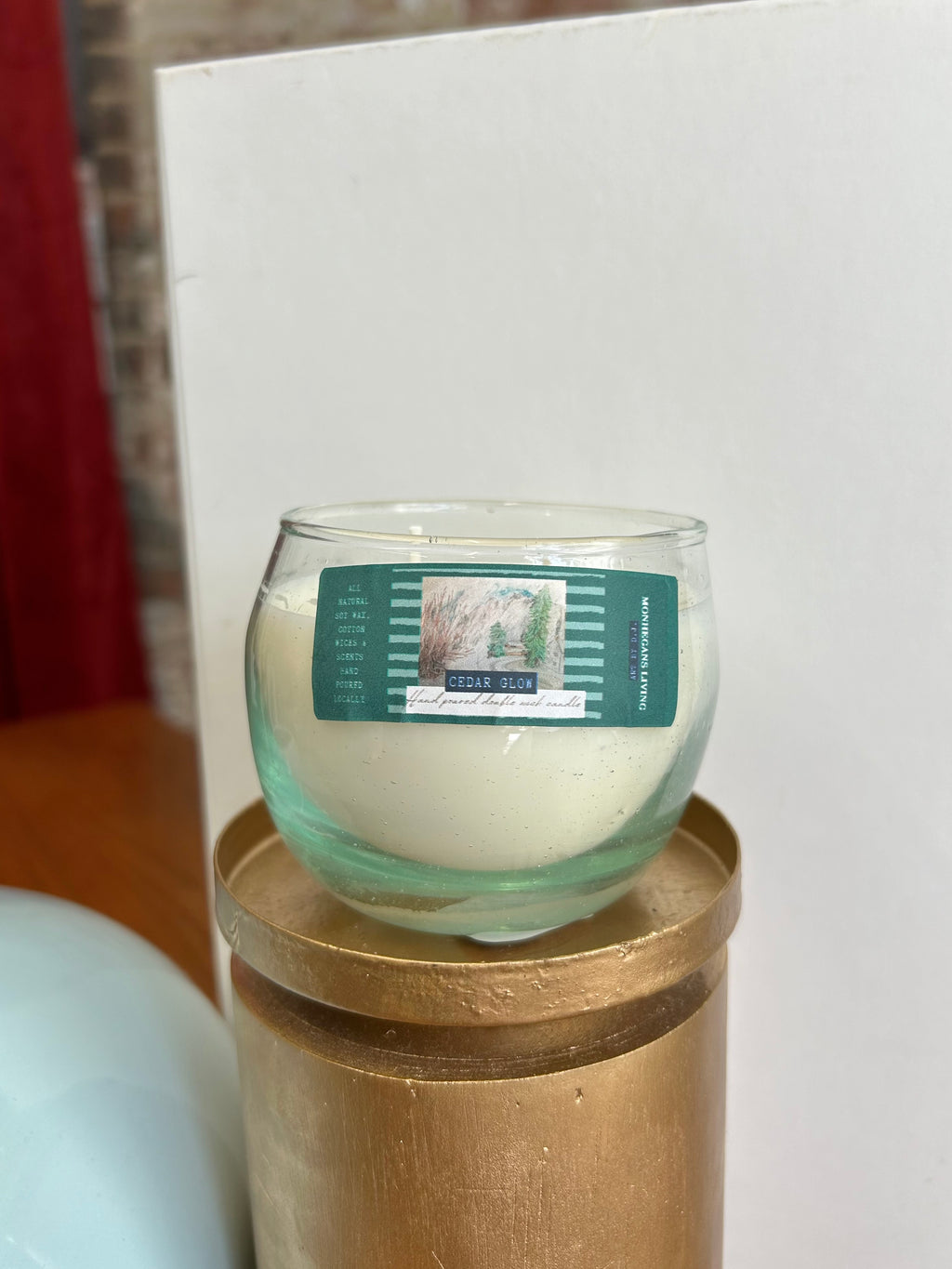 Glass candle with a label on a gold stand against a white background