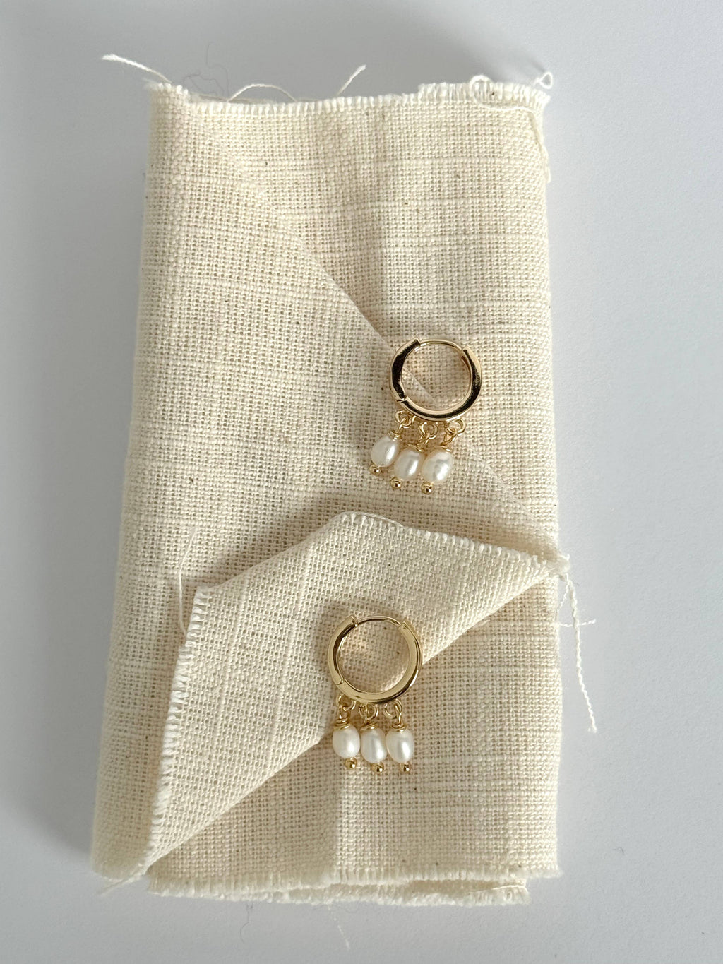 Pair of gold hoop earrings with pearl drops on a textured beige fabric background