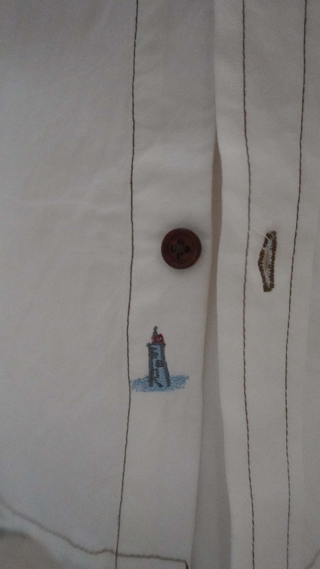 Close-up of a button on a white shirt with a small embroidered design.