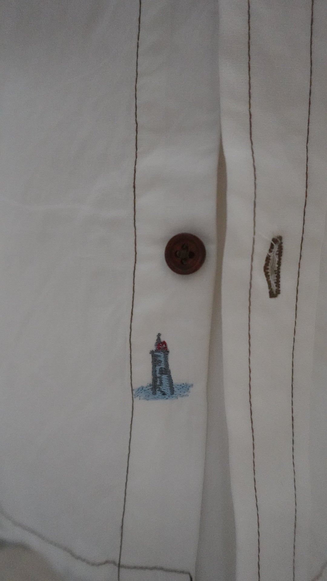 Close-up of a button on a white shirt with a small embroidered design.