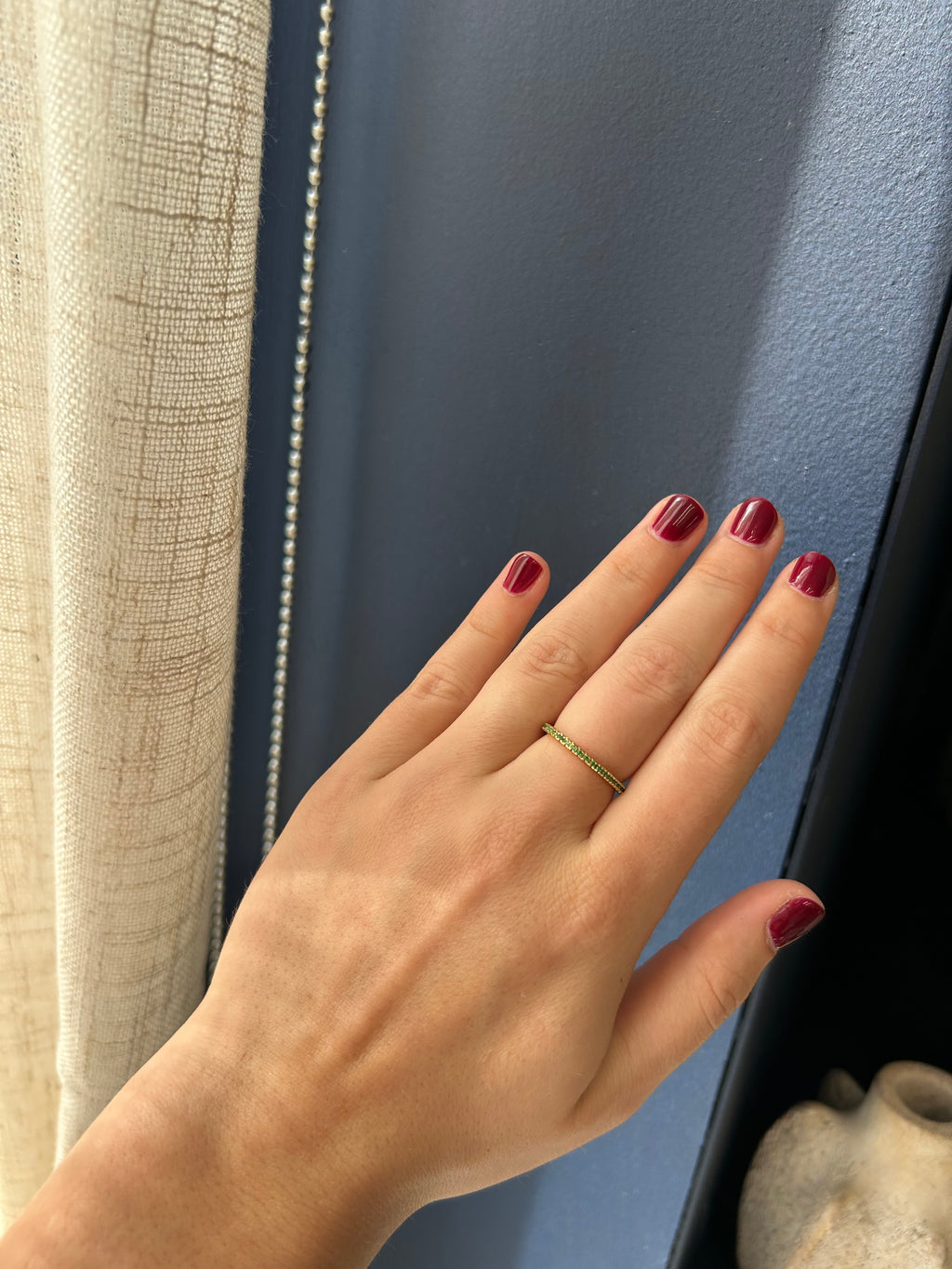 Hand with red nail polish and a gold ring on a blue surface