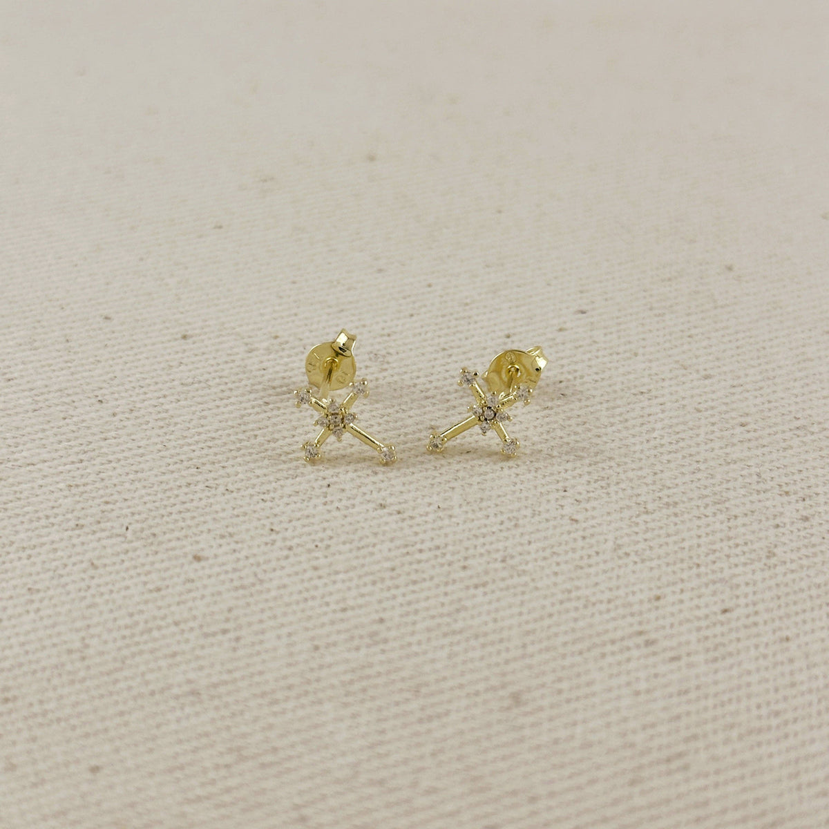 Gold earrings on a beige fabric background
