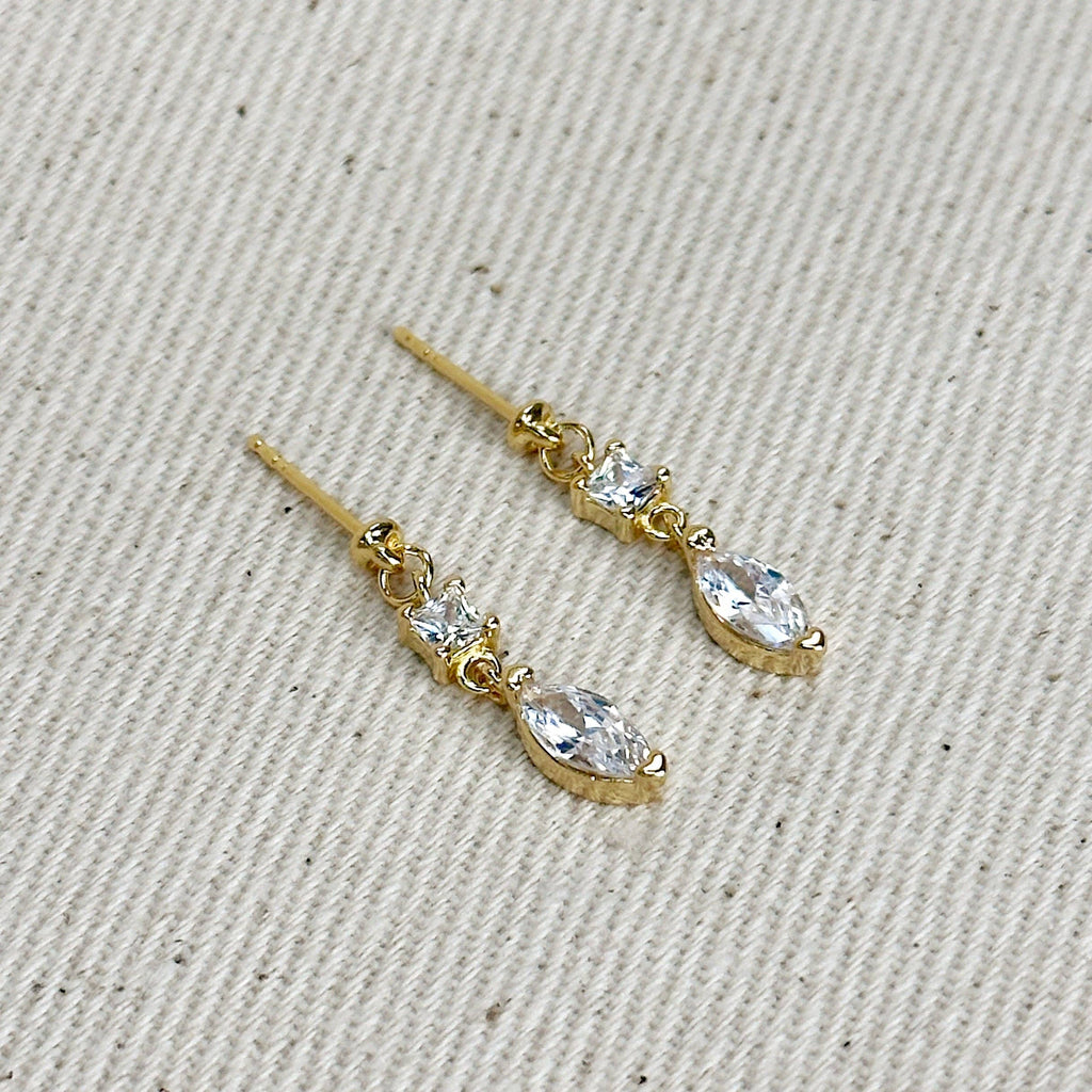 Gold earrings with clear stones on a beige fabric background