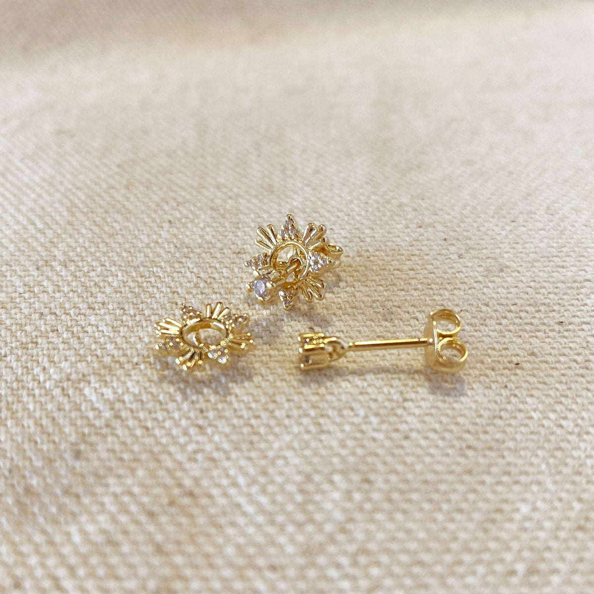 Gold sun-shaped earrings on a beige fabric background